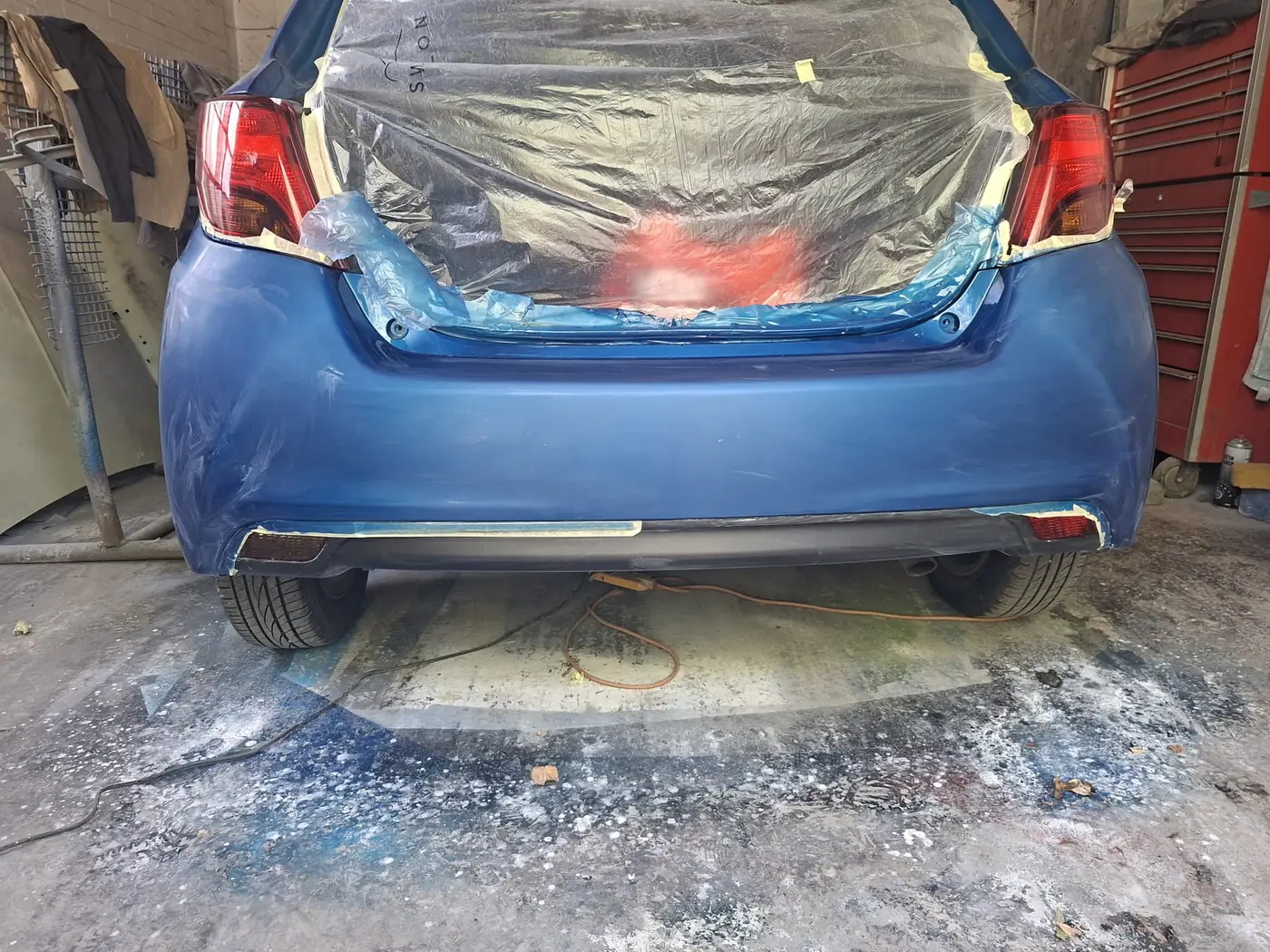 The same blue hatchback with the rear masked and sheeted, prepped for colour